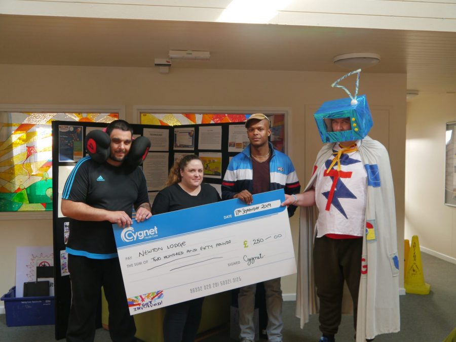 Photo of service users dressed up and holding a cheque.