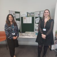 A photograph of two members of the equality and involvement team standing either side of a tabletop exhibition desk displaying posters, leaflets and general information at our annual members meeting 2022.