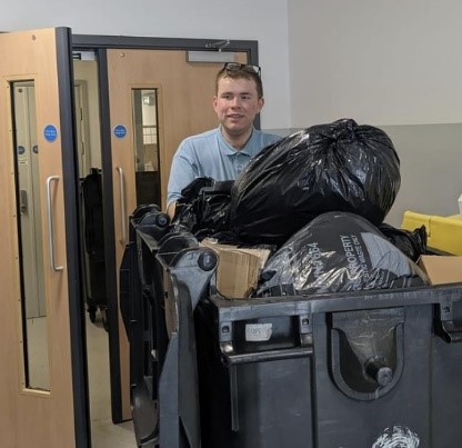 Photo of a man pushing a bin of rubbish