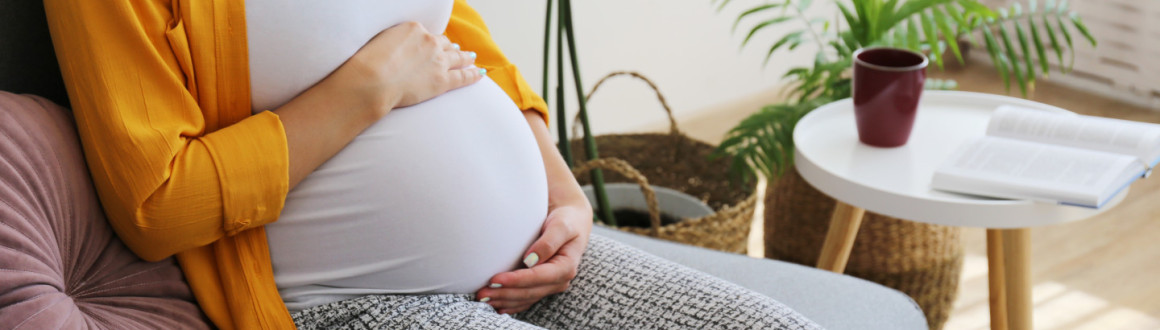 Image of a pregnant lady sat on a sofa holding her tummy, you can't see her face as it is cropped