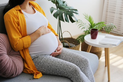 Image of a pregnant lady sat on a sofa holding her tummy, you can't see her face as it is cropped