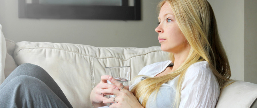 Pregnant lady sat on a sofa drinking coffee looking into the distance