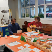 Person sat with guitar and two people sat singing