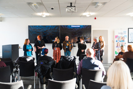 Photo of a group of people stood at the front of a room talking