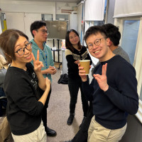 Two people posing with other people talking in background