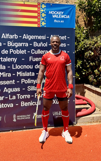 A man dressed in red stands holding a hockey stick and preparing to play.